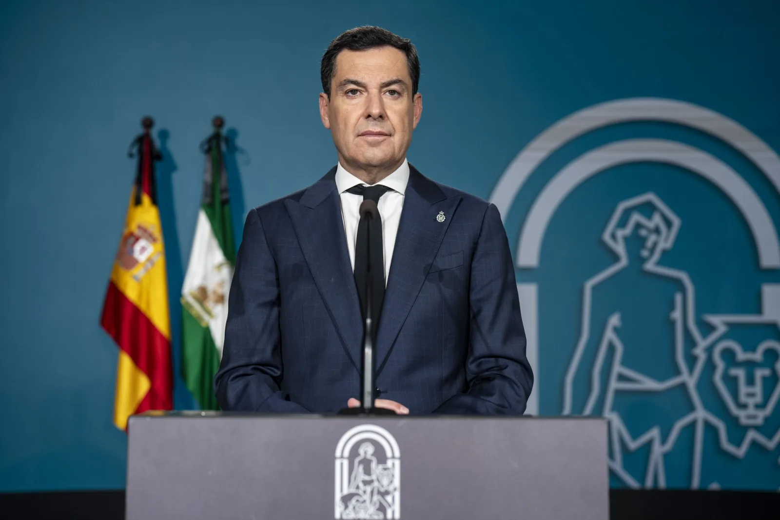 Juanma Moreno, con corbata negra, durante su declaración institucional ante las banderas de España y Andalucía con crespones negros.