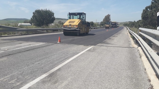 Una carretera cortada con maquinaria amarilla de obras y conos naranjas sobre el asfalto, con barreras metálicas a ambos lados.