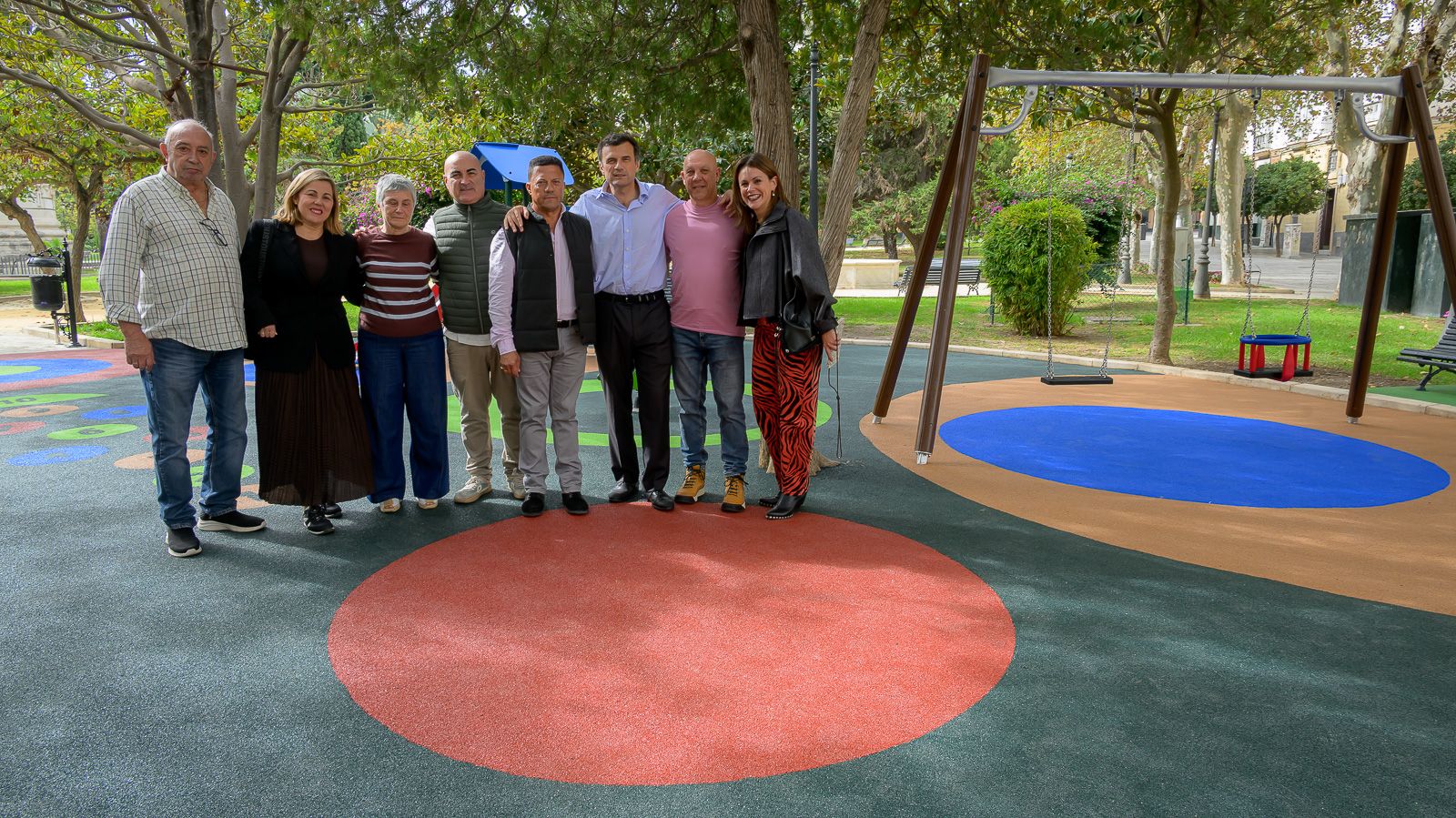 Siete personas posan en grupo sobre un suelo de caucho de colores junto a columpios en un parque.