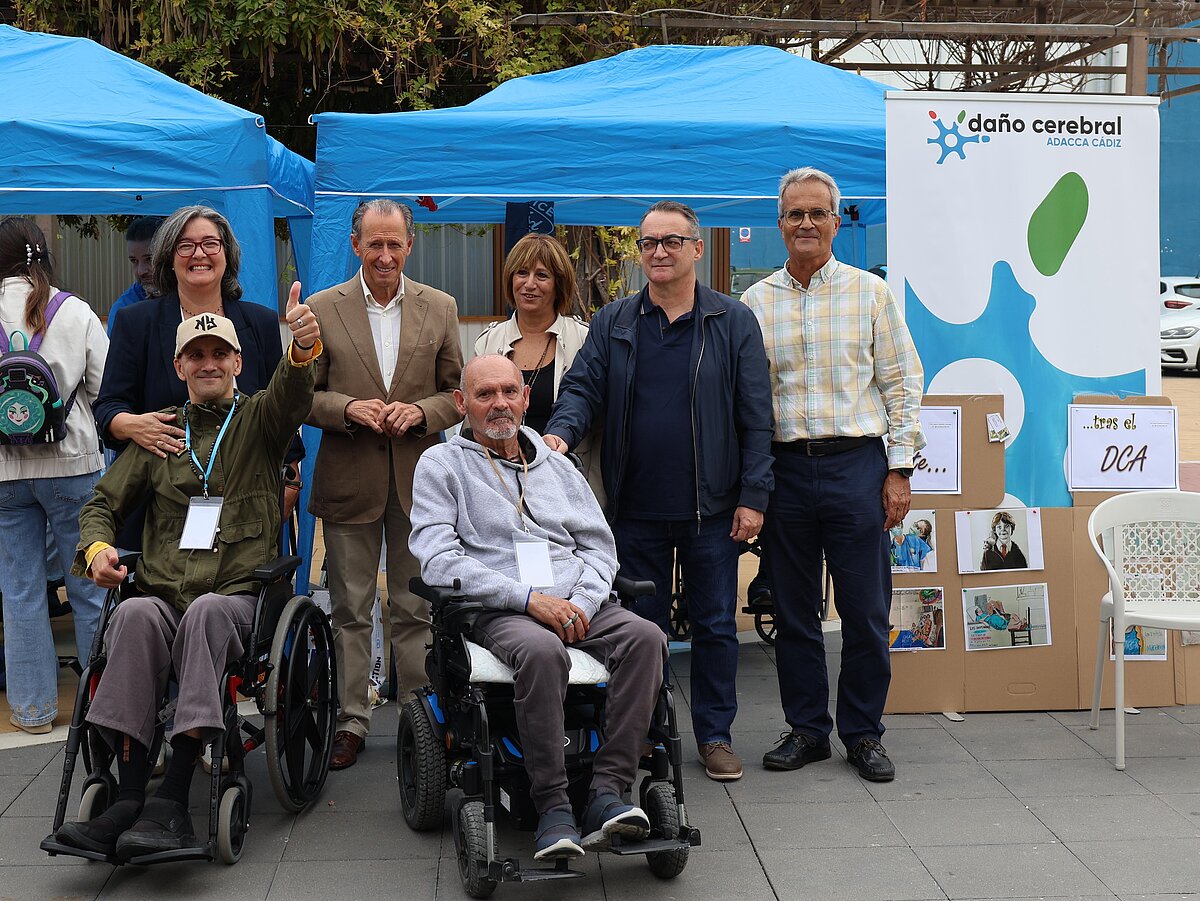 Seis personas posan junto a una carpa azul y un cartel de daño cerebral, dos de ellas en silla de ruedas.