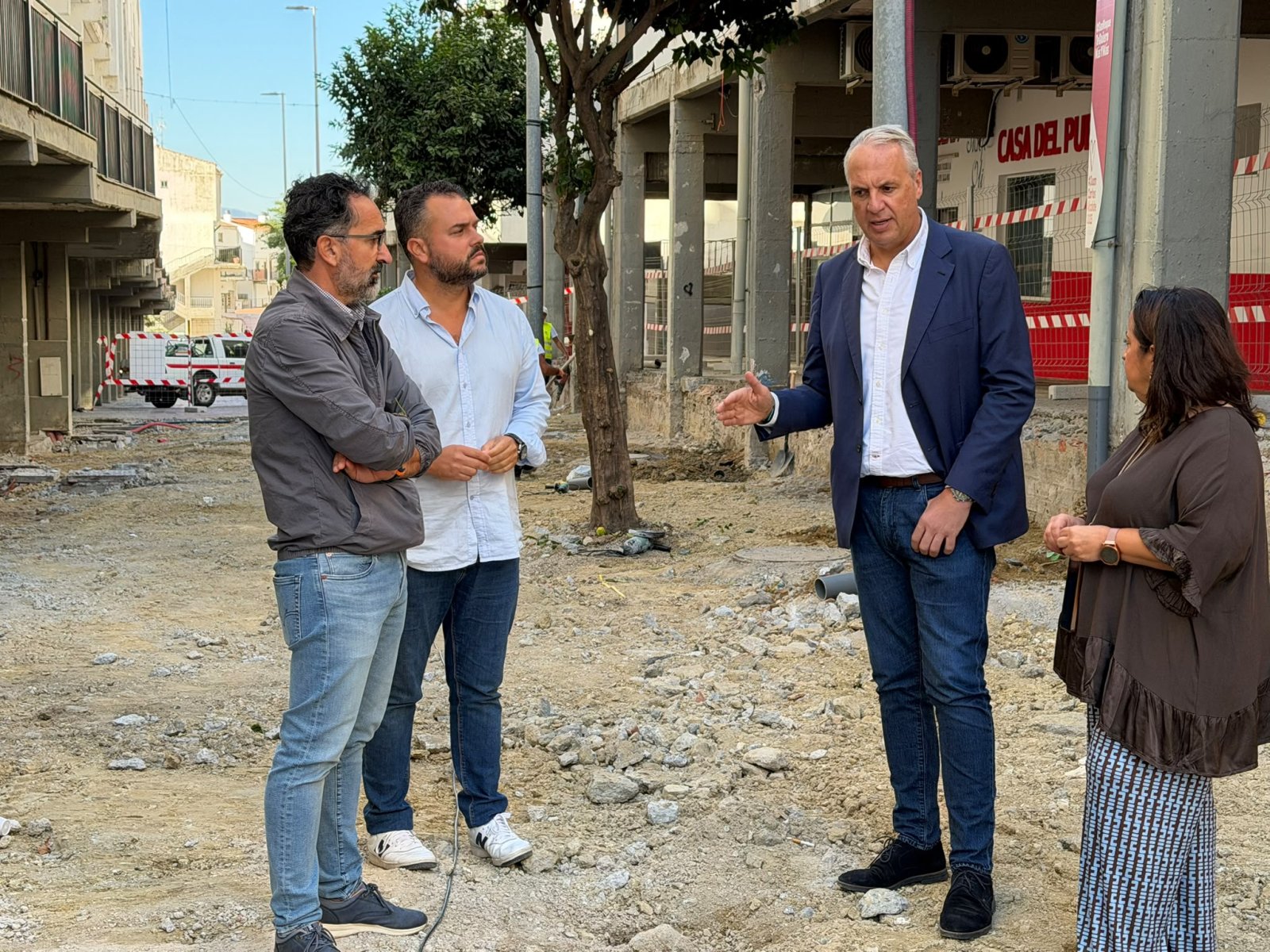 Cuatro personas conversan de pie en una zona de obras con escombros, junto a un edificio en construcción.
