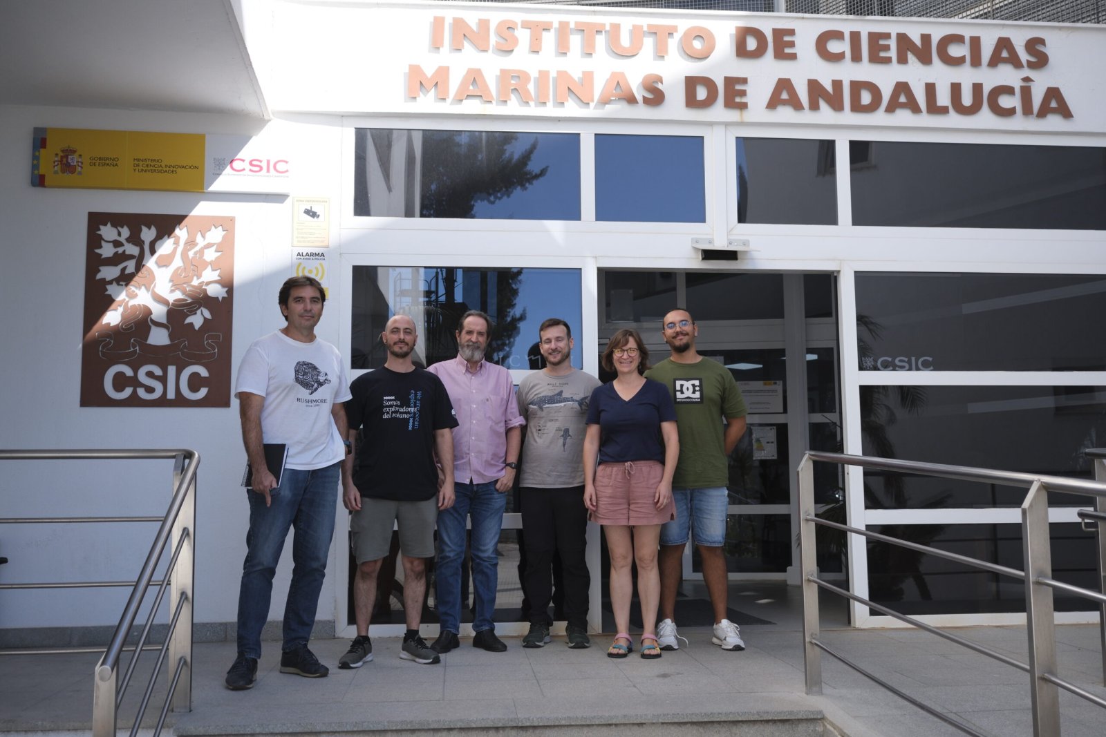 Seis personas posan de pie junto a la entrada de un edificio blanco con el rótulo Instituto de Ciencias Marinas de Andalucía.