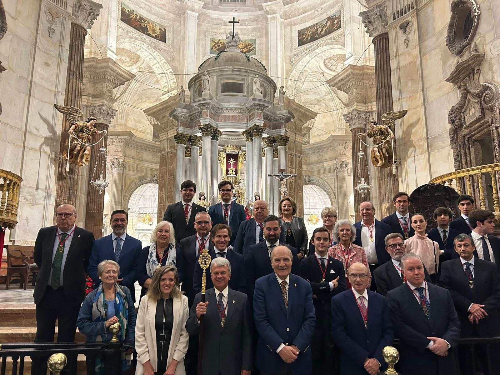 Un grupo de personas trajeadas posa sonriente ante un altar con cúpula y columnas en el interior de una iglesia.