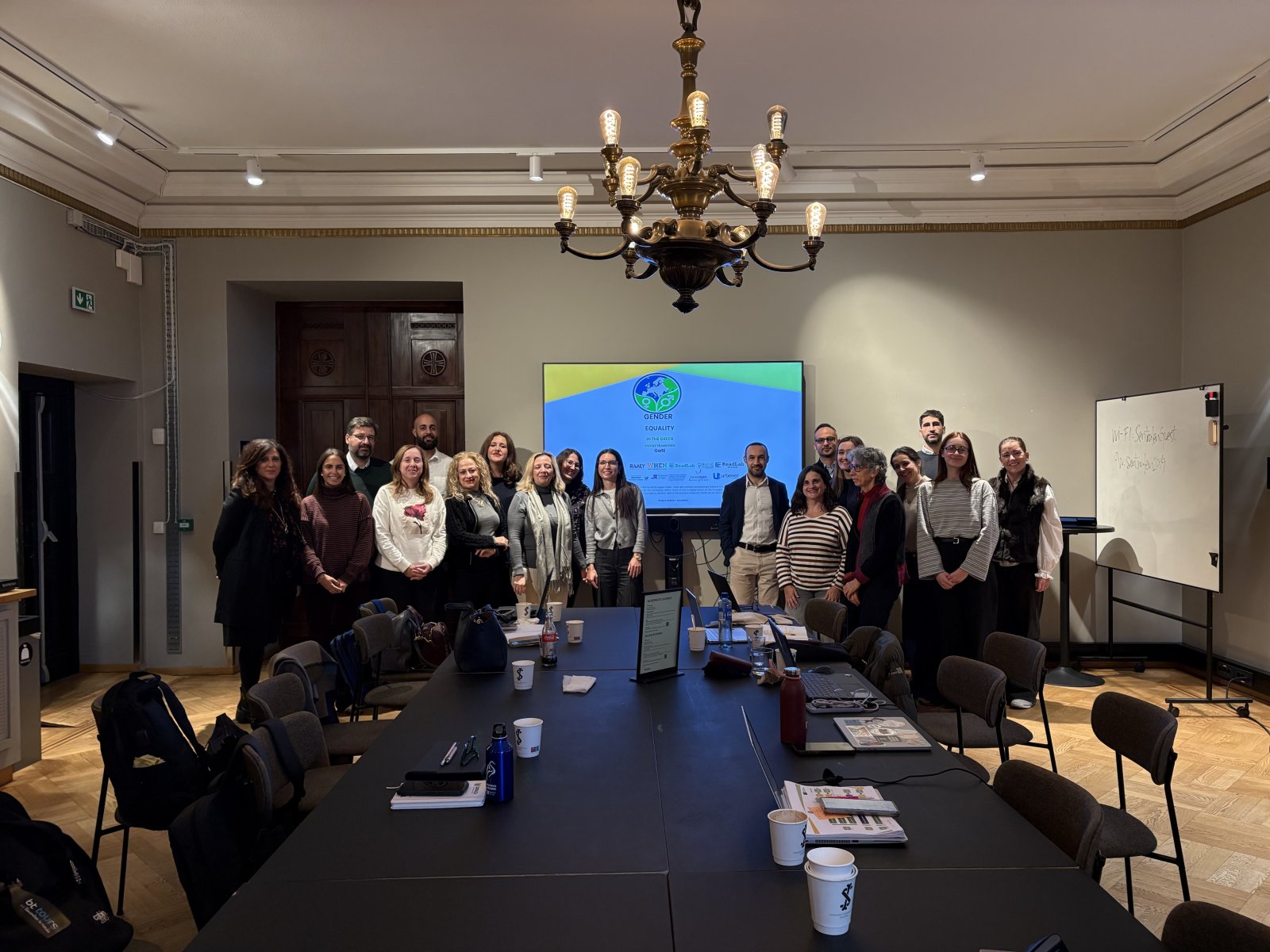 Un grupo de personas posa de pie tras una mesa de reuniones con una pantalla que muestra el proyecto GatE al fondo.