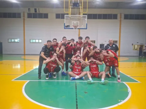 Equipo de baloncesto con camisetas rojas posando en grupo bajo una canasta, en una cancha cubierta de colores verde y amarillo.
