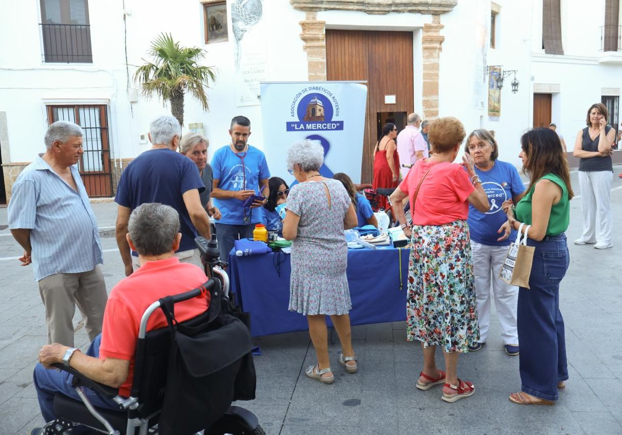 Un grupo de personas conversa alrededor de una mesa con un cartel de una asociación de diabéticos en una plaza.