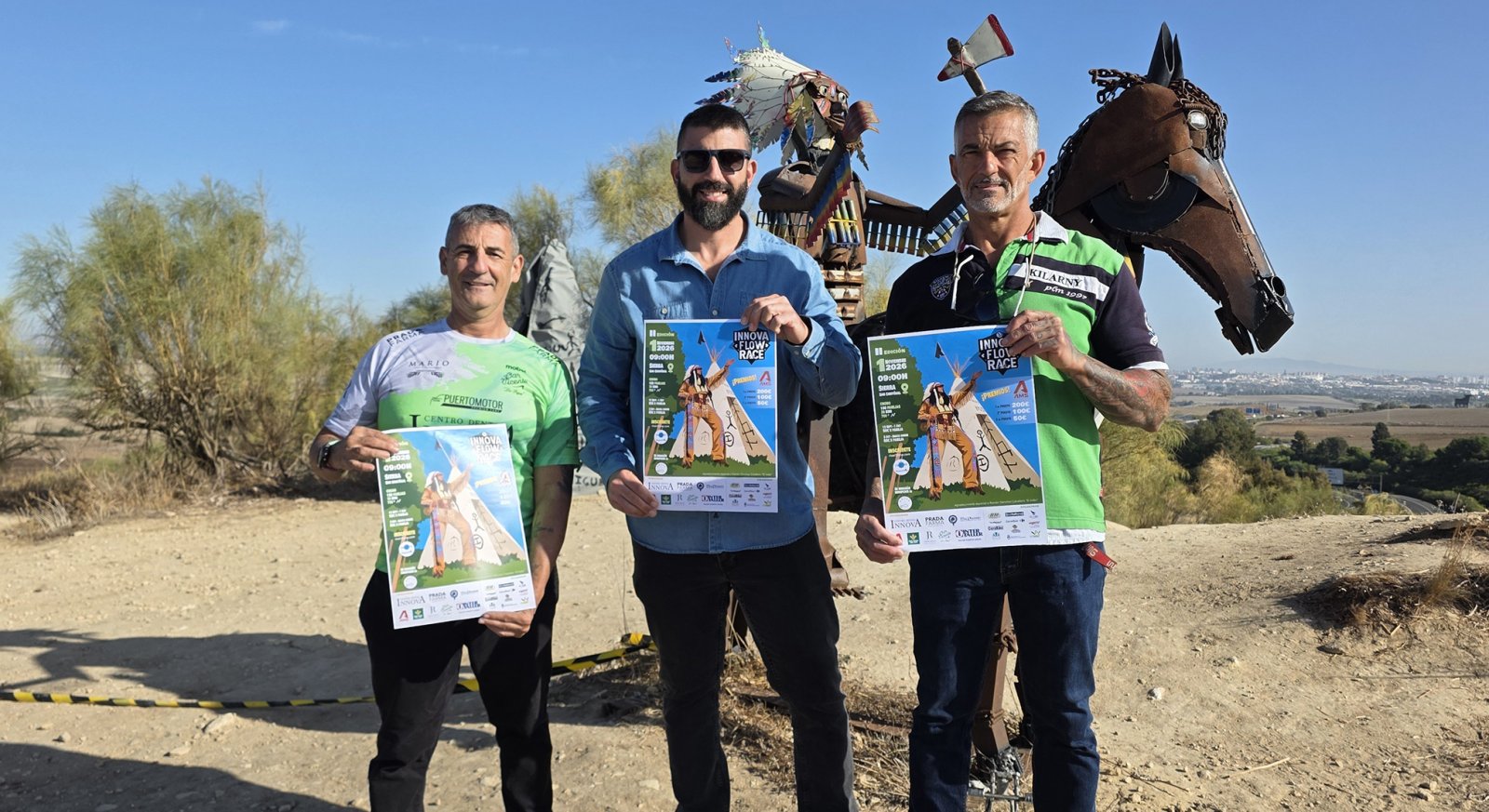 Tres hombres de pie al aire libre sostienen carteles de una carrera junto a una escultura metálica de un caballo.