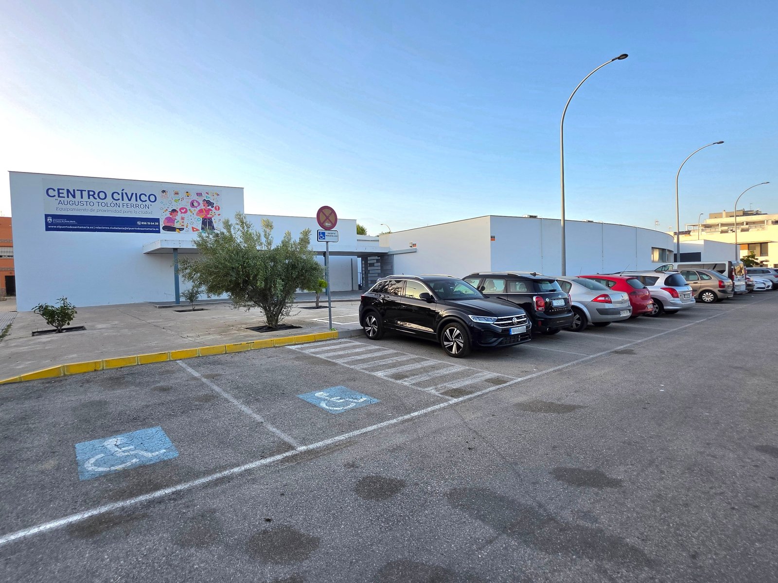 Aparcamiento con plazas para personas con discapacidad frente a un edificio blanco de una planta con un cartel que dice Centro Cívico.